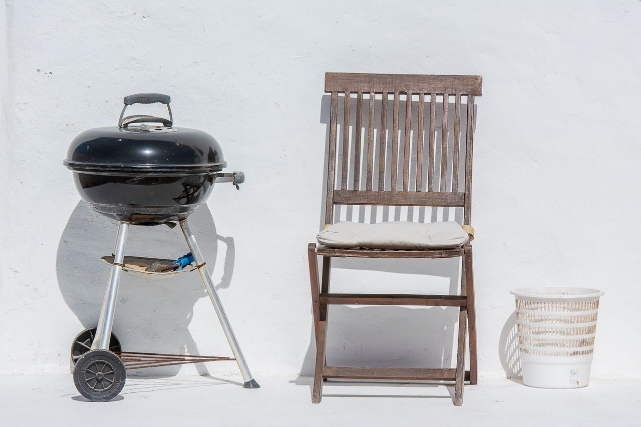 get-in-touch Outdoor scene with a barbeque grill, wooden chair, and white wall, evoking summer relaxation.