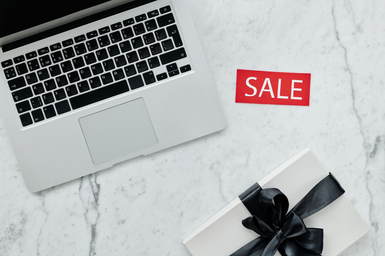 services-06 Top-down view of a laptop and gift with a sale sign on marble background.
